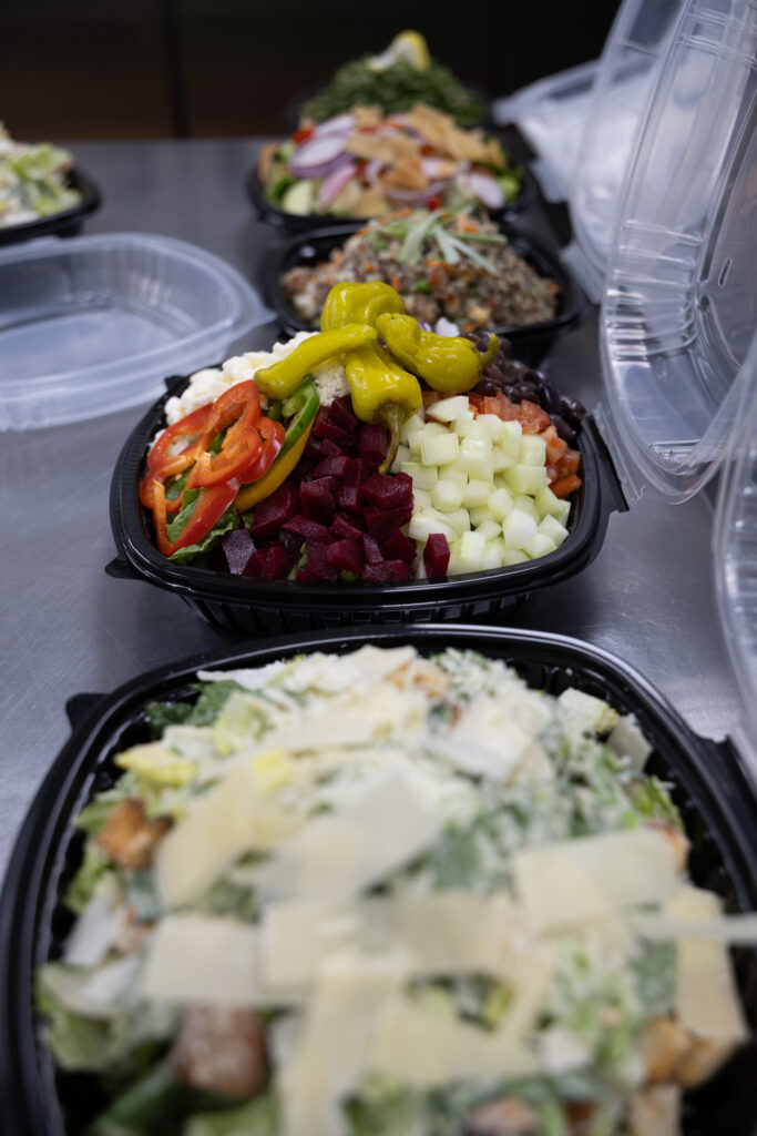 Assorted fresh salads including Greek salad, Fattoush, and garden salads prepared daily at Fire & Feast in Commerce Township, Michigan.