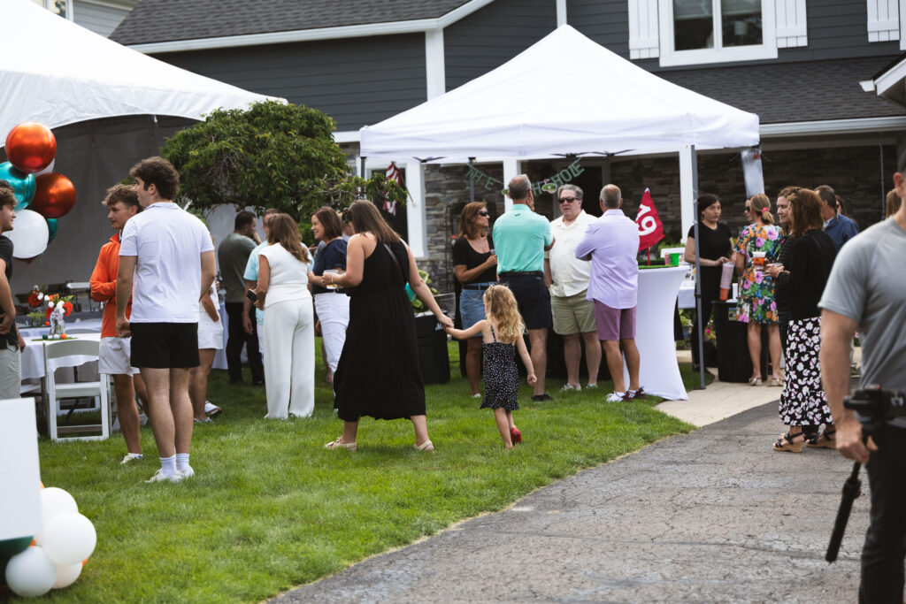 Guests enjoying Fire & Feast catering at an outdoor celebration with tent seating and backyard dining in Commerce Township, Michigan.