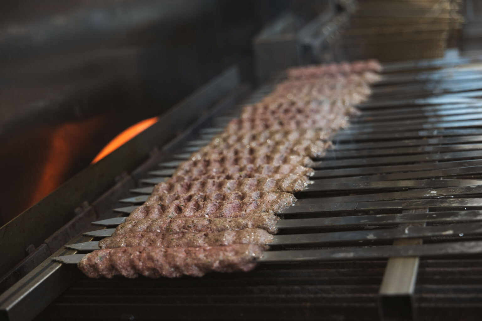 Mediterranean beef and lamb kabobs cooking over a hot char grill at Fire & Feast in Commerce Township, Michigan.